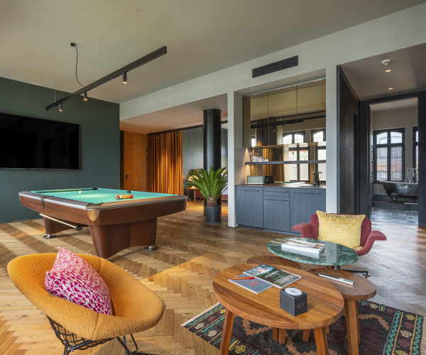 Modern living room with a pool table, a large TV, stylish chairs, a circular coffee table, and wood herringbone flooring.
