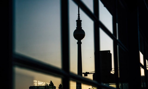 Die Silhouette des Berliner Fernsehturms spiegelt sich bei Sonnenuntergang in den Glasfenstern, im Vordergrund ist ein klares Gittermuster zu erkennen.