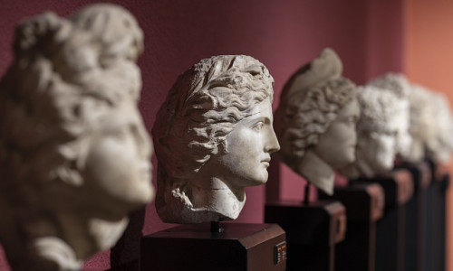 Eine Reihe antiker Marmorbüsten männlicher Figuren, die auf dunklen Sockeln vor einer rötlichen Wand ausgestellt sind.