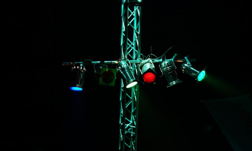 Bühnenlichter in Blau, Grün und Rot leuchten von einer Metallfachwerkkonstruktion vor einem dunklen Hintergrund.