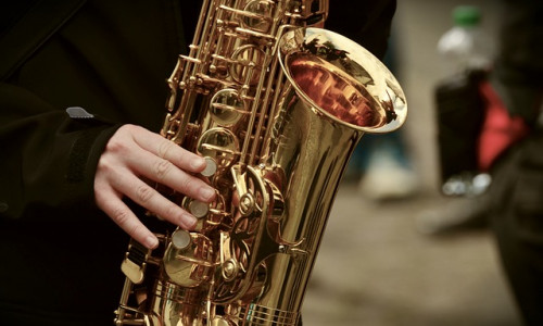 Eine Person, die ein glänzendes Messingsaxophon spielt, wobei ihre linke Hand auf den Tasten des Instruments liegt.